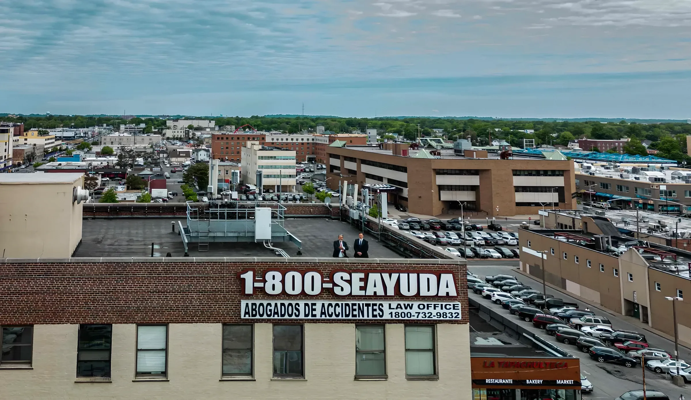 Vista aérea del edificio de 250 Fulton Avenue, en Hempstead, con el letrero 1-800-SEAYUDA Abogados de Accidentes.
